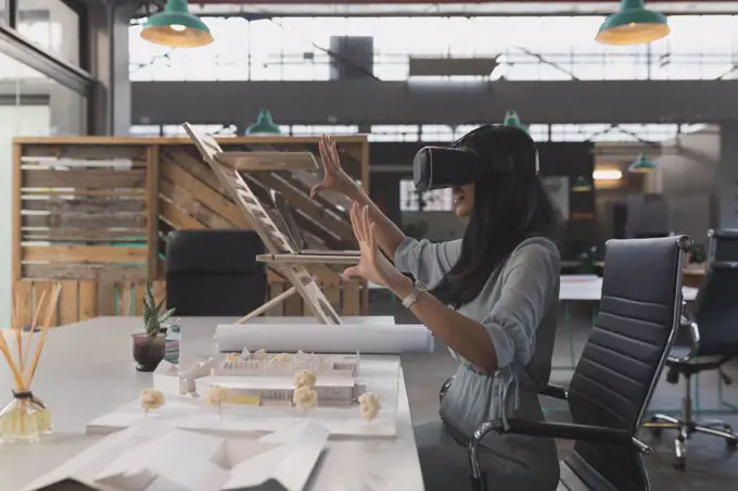 Female executive using virtual reality headset at table in office