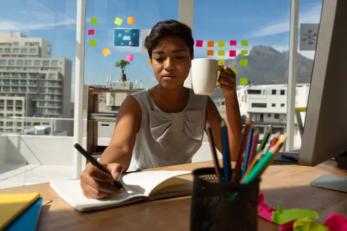 Business executive having coffee while writing on diary in office