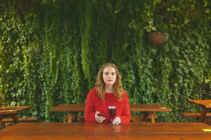 Redhead woman using mobile phone while having beer in outdoor cafe