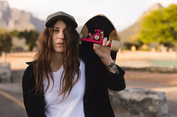 Portrait of female skateboarder carrying skateboard on shoulders