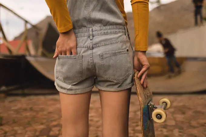 Mid section of female skateboarder standing with skateboard