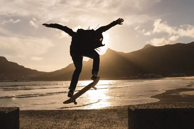 Silhouette of woman skateboarding on wall at beach