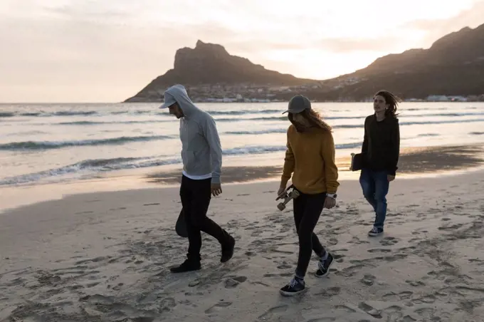 Young skateboarders walking on the beach during sunset