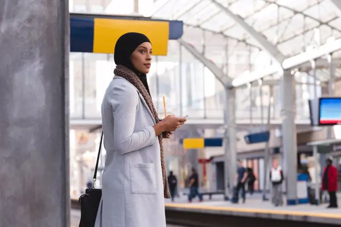 Hijab woman waiting for train while using mobile phone at railway station