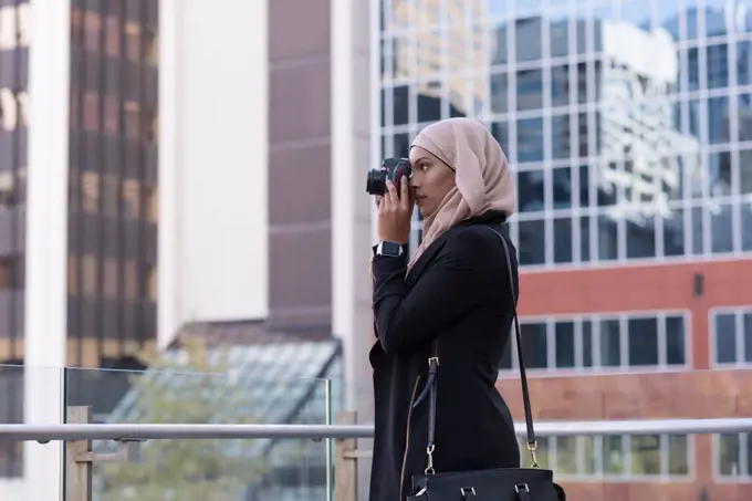 Hijab woman clicking photo in digital camera at balcony