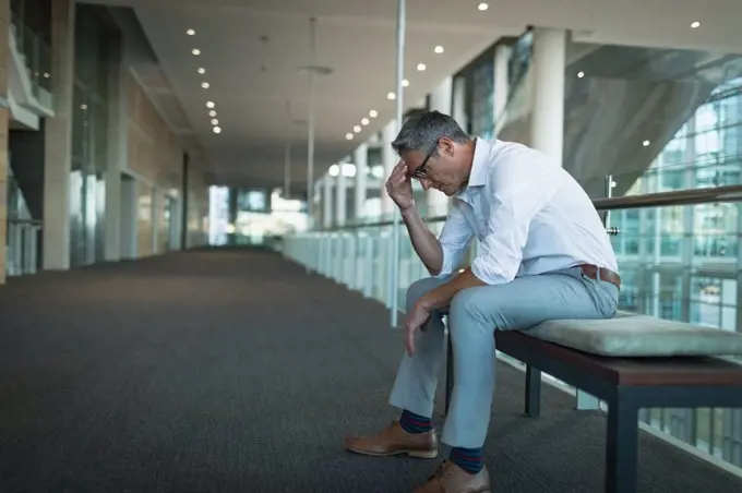 Side view of frustrated businessman sitting on the bench in office