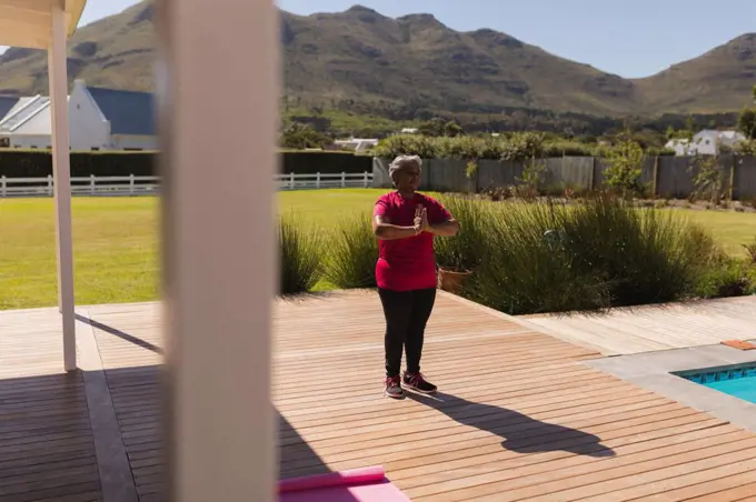 Front view of an active senior  African American woman performing yoga next to the swimming pool in the backyard of home