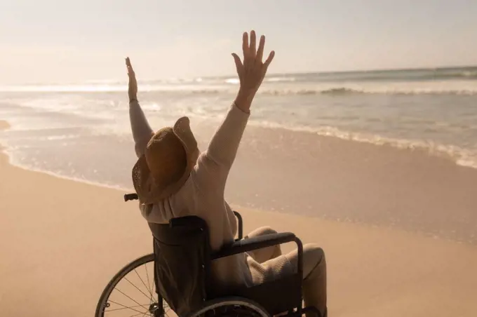 Rear view of active disabled senior woman with arms up on the beach