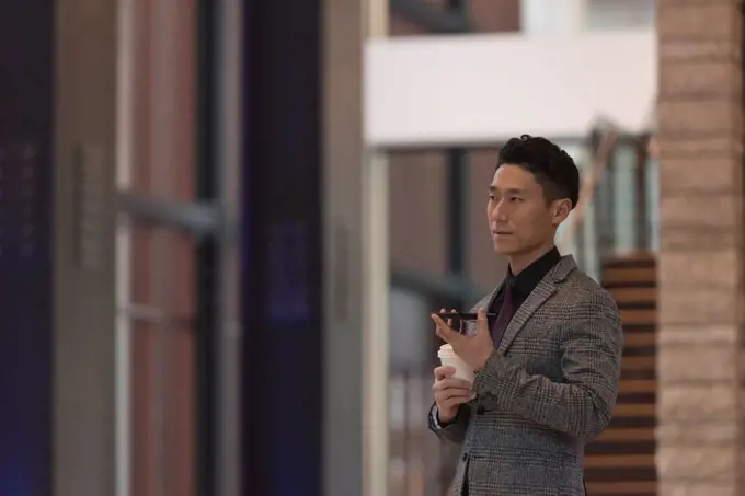 Side view of businessman holding mobile phone while having coffee in the modern office