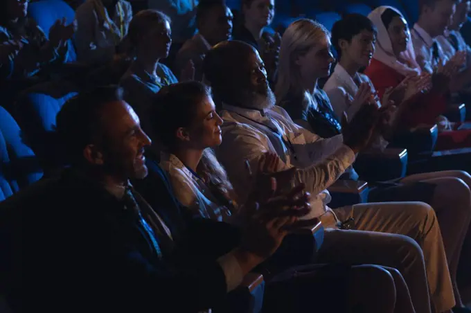 Side view of mixed race business colleagues sitting and watching presentation with audience and clapping hands