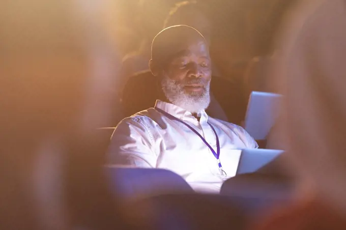 Front view of old African-American businessman looking at digital tablet while sitting in the auditorium 