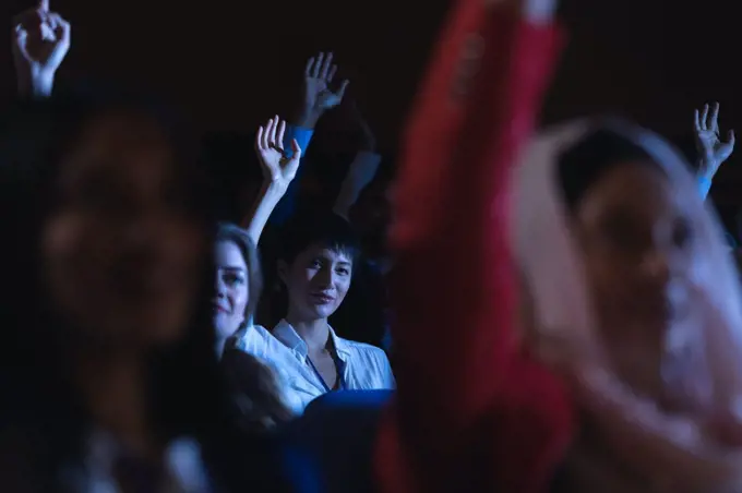 Low angle view of beautiful Asian businesswoman sitting and raising hand while sitting in auditorium