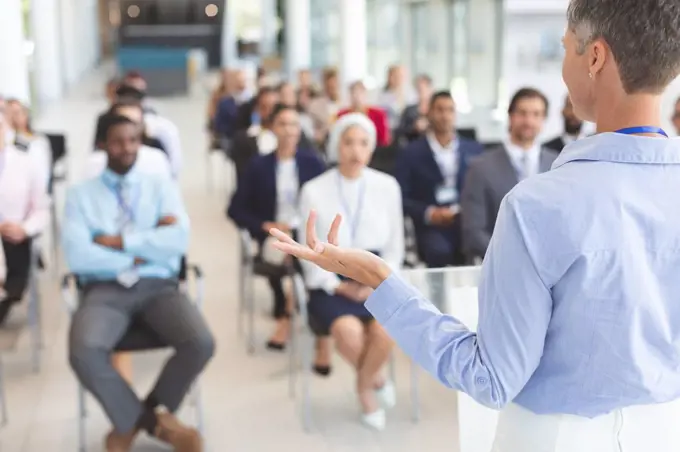 Rear view of  Caucasian female speaker speaks to diverse business people  in a business seminar in conference