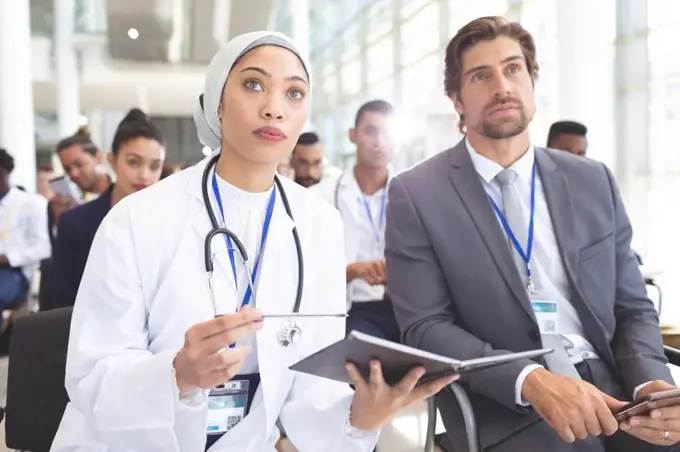 Front view of mixed race female doctor with Caucasian  businessman attending seminar in office. She holding a notebook