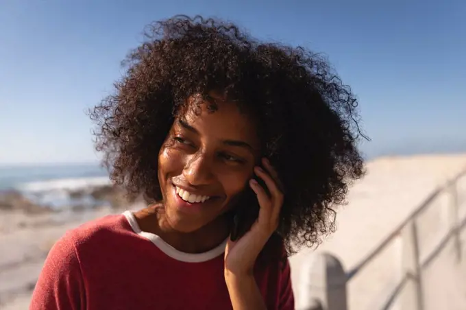 Close up of African-american woman talking on mobile phone while smiling at beach 