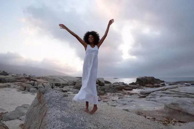 Low section of African-american woman standing with opened arm near sea side in dusk