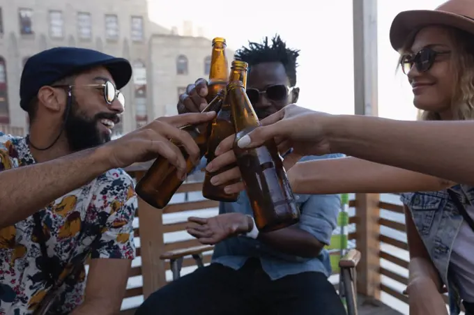 Front view of group of diverse friends toasting with beer bottles at home in balcony 