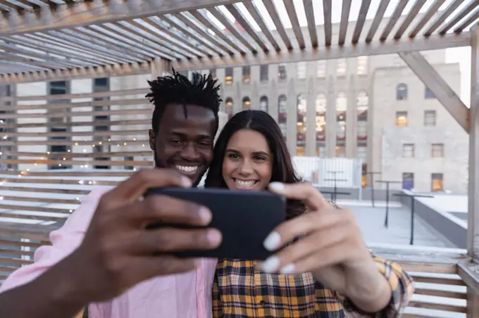 Front view of multi ethnic  couple taking selfie in balcony at home 