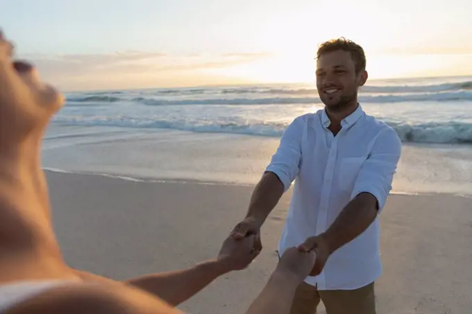 Side view of young Caucasian love couple holding hand while standing at beach on a sunny day. They are emjoying their holidays