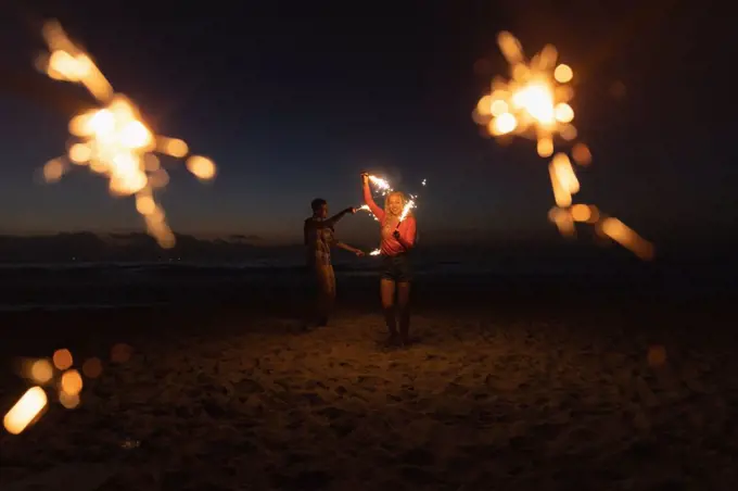 Front view of young Caucaisan couple playing with sparkler at beach. They are enjoying their holidays