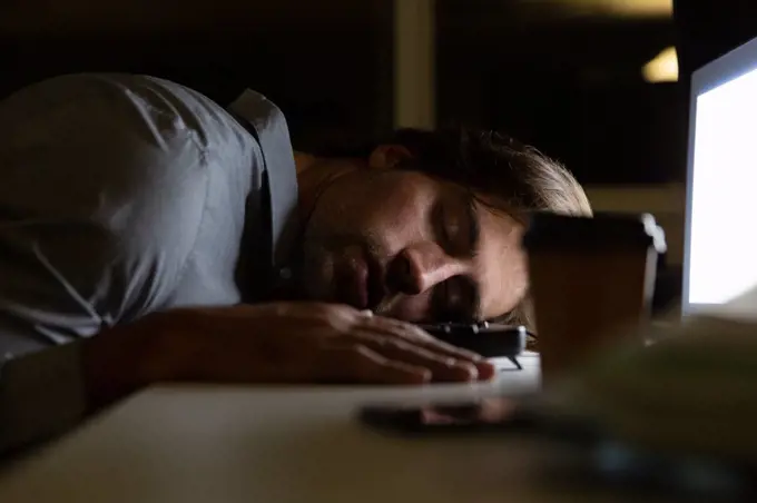 Side view of young Caucasian male executive sleeping at desk in a modern office