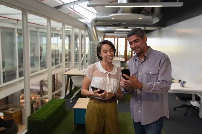 Front view of multi ethnic business people standing in the office while discussing about their mobile phone