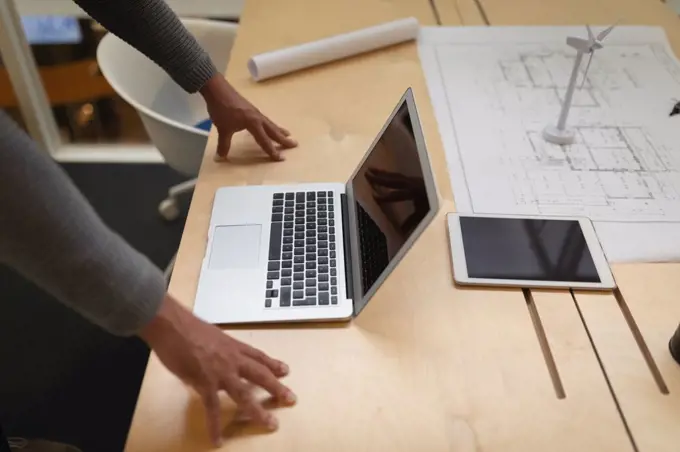 Mid section of a businessman leaning on the desk and looking at his laptop