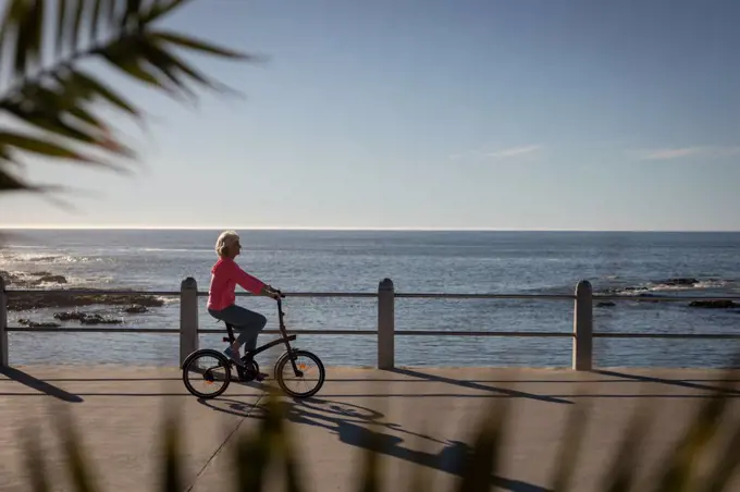 Side view of an active senior woman riding bicycle on a promenade along the beach on the evening