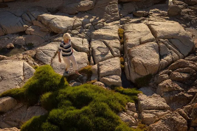 High angle view of an active senior woman walking on the rock at beach on the evening