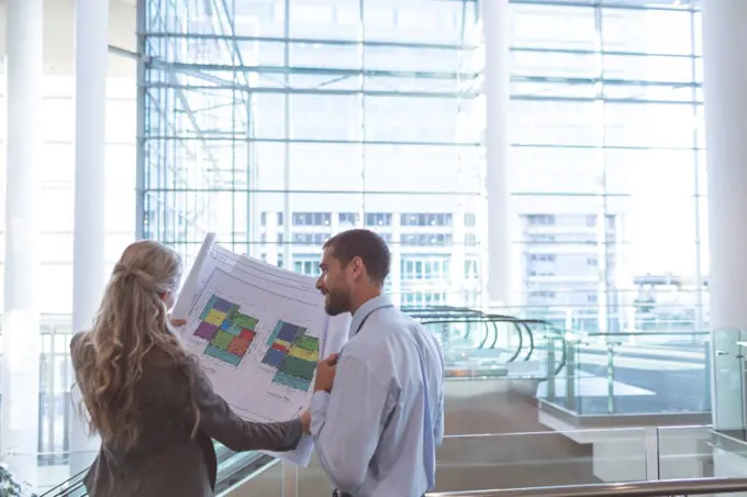 Rear view of business people discussing over blueprint in a modern office building