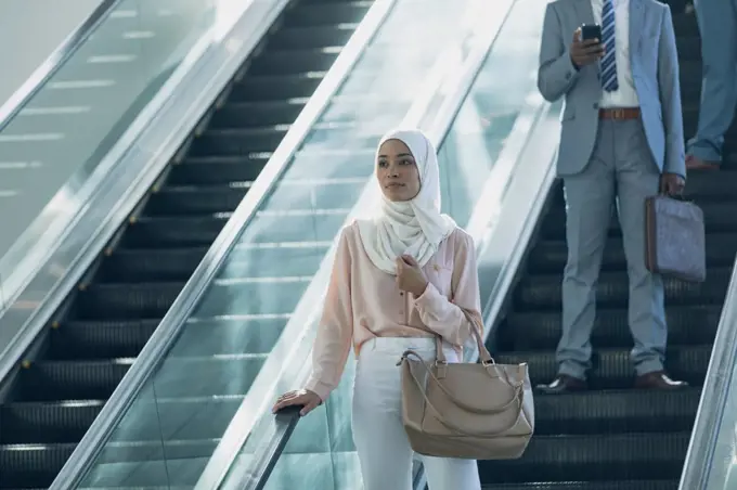 Front view of businesswoman in hijab using escalators in modern office 