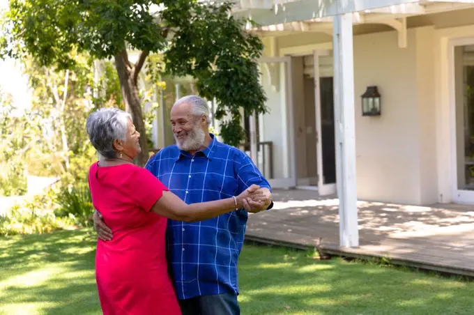 Self isolation in quarantine lock down. side view of a senior mixed race couple at home in the garden outside their house on a sunny day, dancing together and smiling