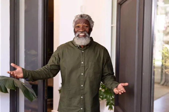 Senior African American man enjoying his time at home, opening front doors, greeting a visitor, looking at the camera and smiling