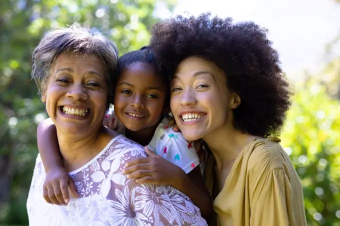 Multi-generation mixed race family enjoying their time at a garden, a senior woman is holding her granddaughter piggy back, looking at the camera and smiling