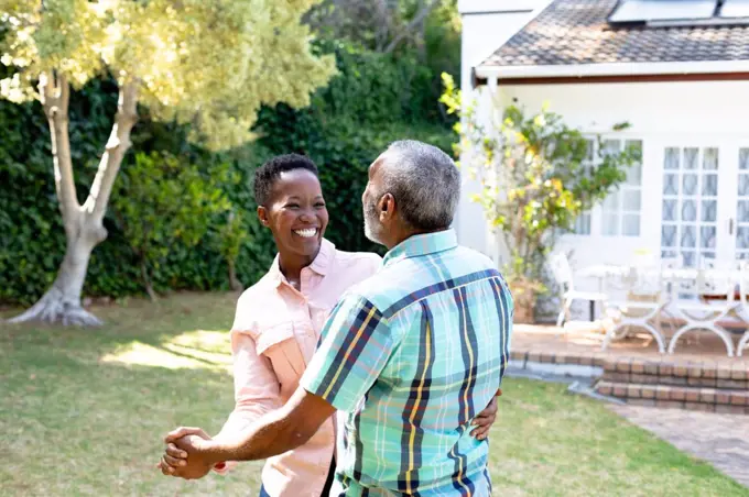 Senior African American couple spending time in their garden on a sunny day, dancing on a lawn. Social distancing and self isolation in quarantine lockdown.