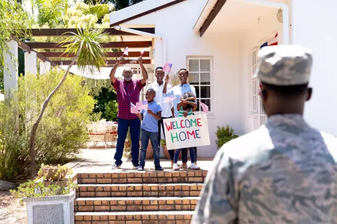 African American three generation family standing by their house with a banner, welcoming an African American solider wearing uniform.