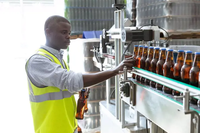 African American man worker working in a brewery, inspecting the bottles at a conveyor belt. Manufacturing and beer brewery. 