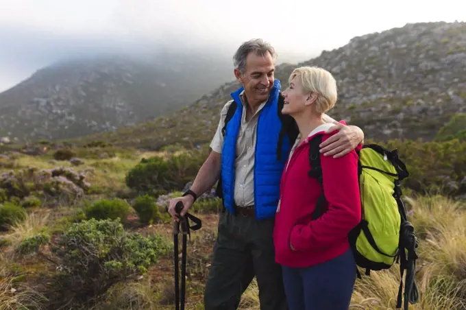 Senior couple spending time in nature together, walking in the mountains, man is embracing the woman, looking and each other and smiling. healthy lifestyle retirement activity.