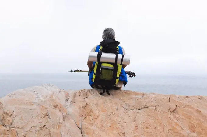 Senior man spending time in nature, walking in the mountains, sitting on a rock and enjoying the view. healthy lifestyle retirement activity.