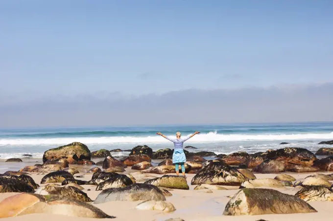 Senior woman spending time in nature, walking on the beach, enjoying the view, raising her arms. healthy lifestyle retirement activity.