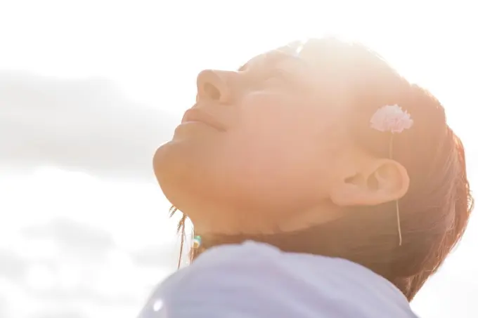 Woman with flower behind ear looking up to sky on a sunny day 