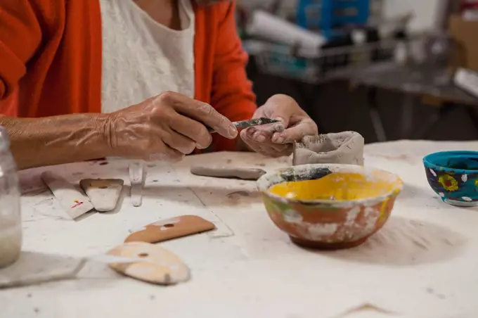 Mid-section of senior woman shaping a clay pot in class