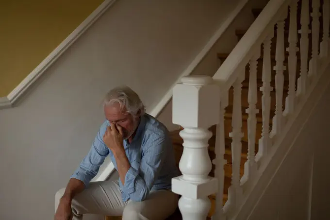 Worried senior man sitting on stairs at home