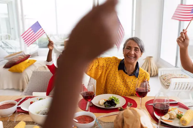 Side view of Multi-generation African American family holding American flag and having celebration on a dining table at home