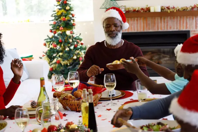 Multi generation african american family in dining room, wearing santa hats. quality family time christmas celebration.