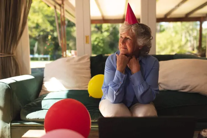 Senior caucasian woman spending time at home celebrating a birthday, wearing party hat and using laptop. self isolation at home during coronavirus covid 19 quarantine lockdown.