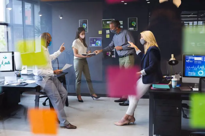 Diverse businessmen and businesswomen wearing face masks working in office. social distancing in business office workplace during covid 19 coronavirus pandemic.