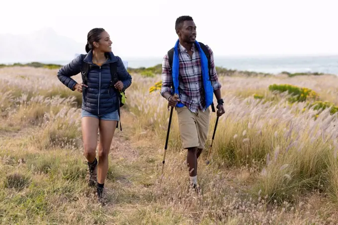 Fit african american couple wearing backpacks nordic walking on coast. healthy lifestyle, exercising in nature.