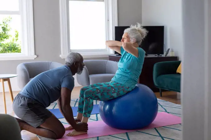 Senior mixed race couple wearing sports clothes exercising in living room. staying at home in self isolation during quarantine lockdown.