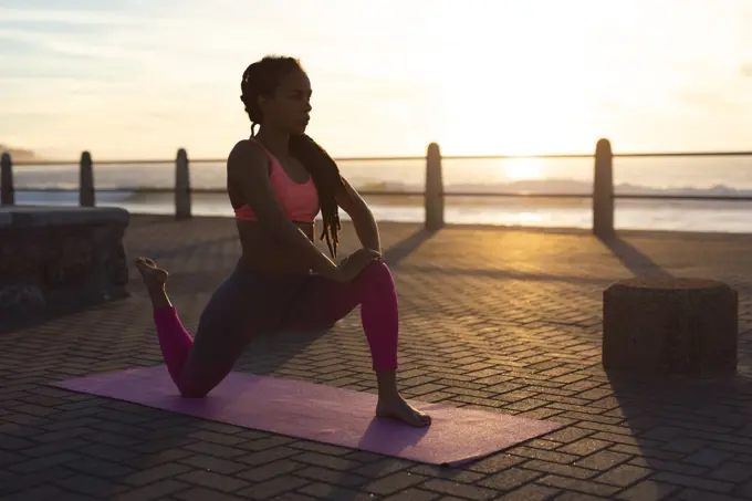 African american woman exercising on promenade by the sea doing yoga. fitness healthy outdoor lifestyle.